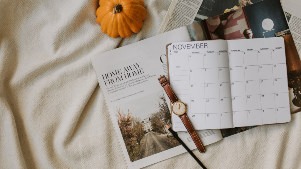 A November calendar spread out on a cozy fabric with a wristwatch and a fall-themed magazine nearby, symbolizing planning and scheduling during the wedding off-season.