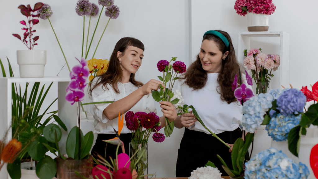 Two florists working together on vibrant floral arrangements, emphasizing teamwork and the importance of administrative and creative collaboration in a wedding business.