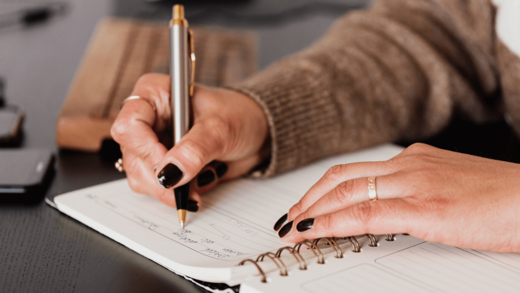 A person writing in a spiral planner, organizing business goals and priorities.