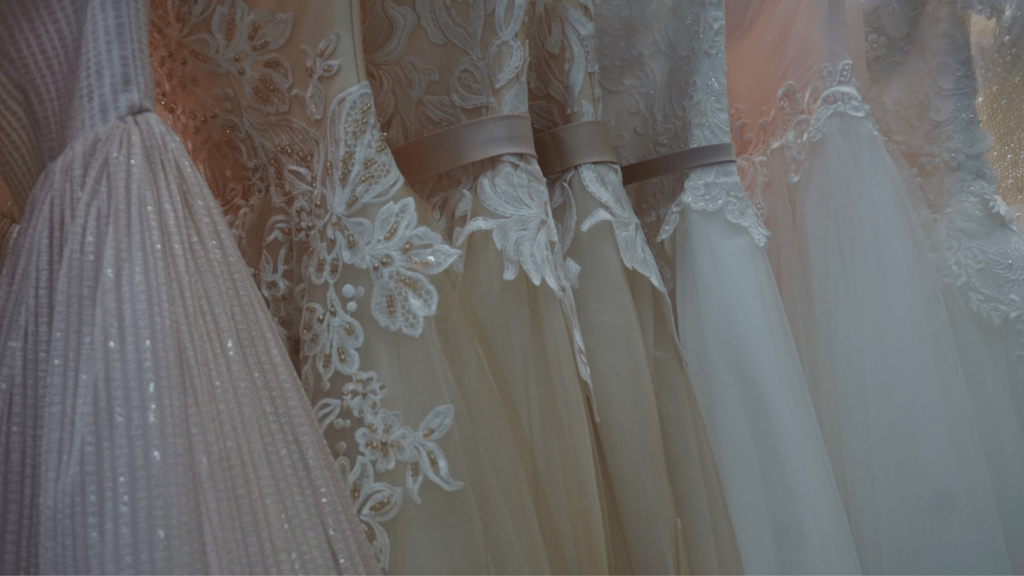 A close-up view of a row of elegant wedding dresses featuring intricate lace details, satin ribbons, and shimmering fabrics.