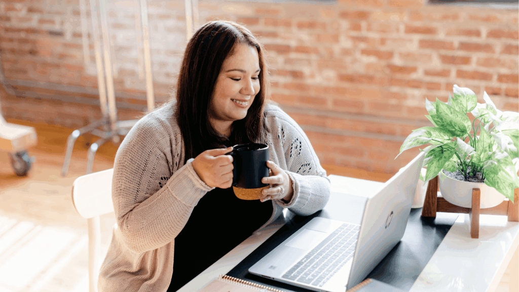 Creative business strategist smiling with coffee while working on laptop, representing approachable client support.