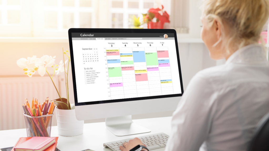 A person is sitting at a desk in front of a computer, viewing a weekly calendar with colorful blocks of tasks scheduled throughout the week. Next to the calendar is a to-do list with tasks like "Write a weekly newsletter," "Sales presentation," and "Review draft."