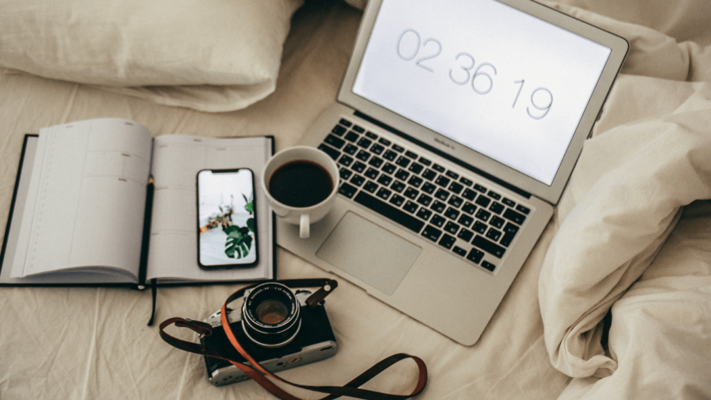 A workspace setup with a camera, laptop, coffee, and a notebook, symbolizing the work of a photographer managing deadlines and projects.