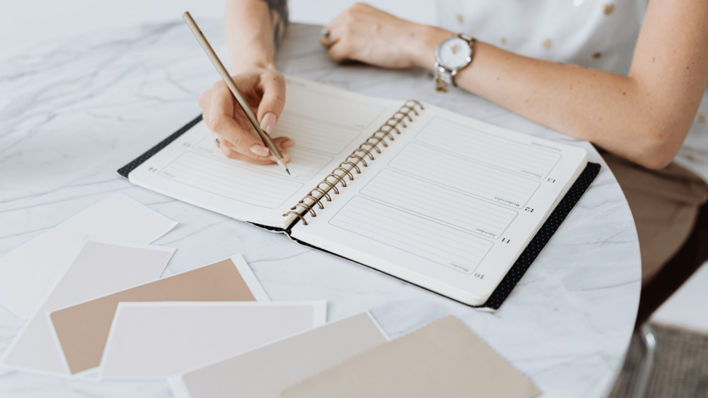 Person writing in a business planner with color swatches on the table, representing organized business operations and planning.