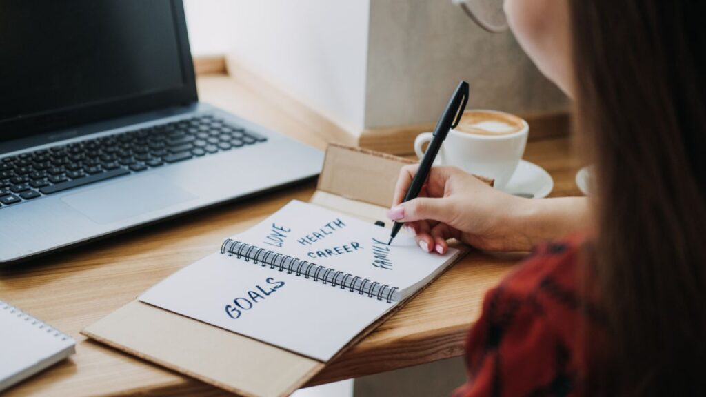 A notebook with handwritten goals including 'Love,' 'Health,' 'Career,' and 'Family,' placed next to a laptop and a coffee cup, representing the goal-setting process for personal and business growth.