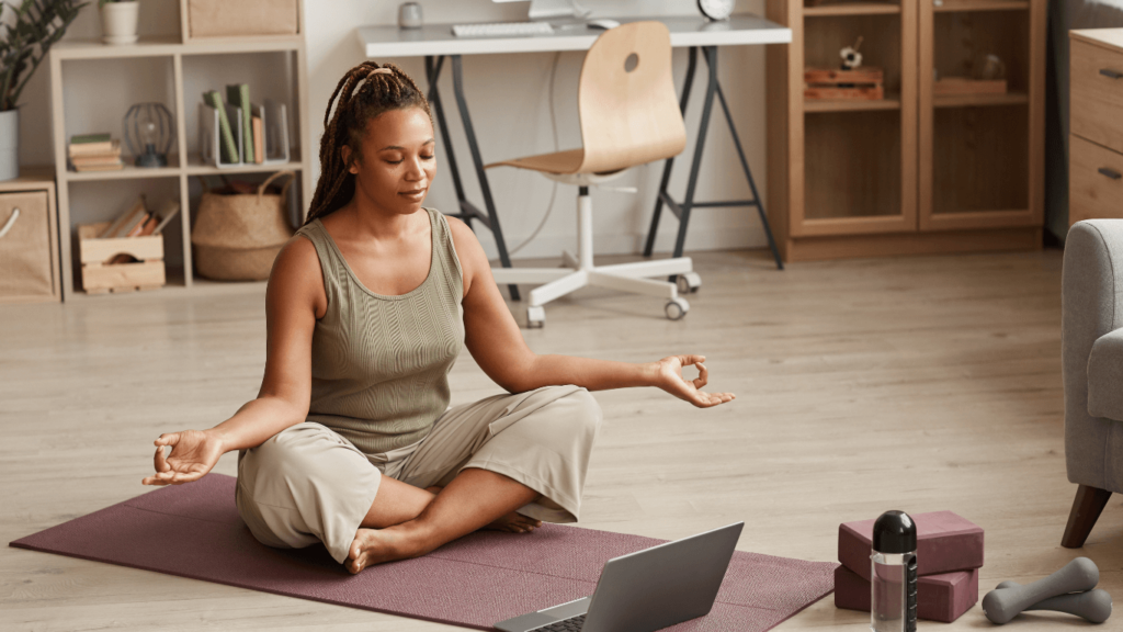 Woman practicing yoga at home, sitting on a mat in a calm workspace, emphasizing work-life balance.