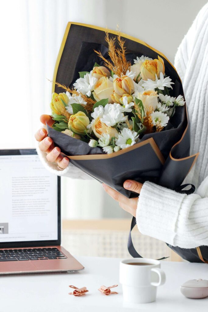 seasonal flowers wrapped in black paper for small business sales online with a computer and coffee on desk