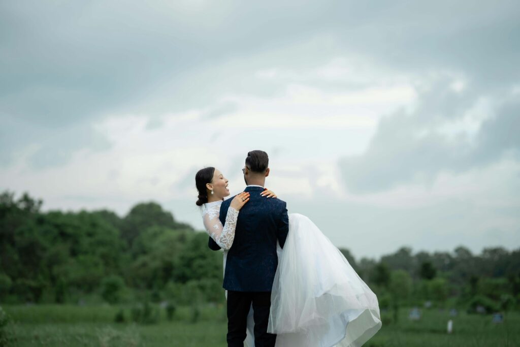 wedding photography couple in a green field on an overcast day. The groom is lifting up the bride and looking to the mountains