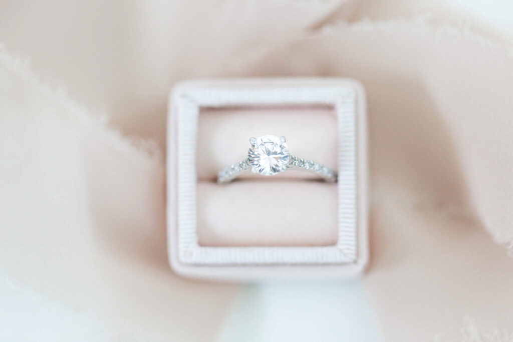 Elegant diamond engagement ring in a velvet box with a soft neutral background.