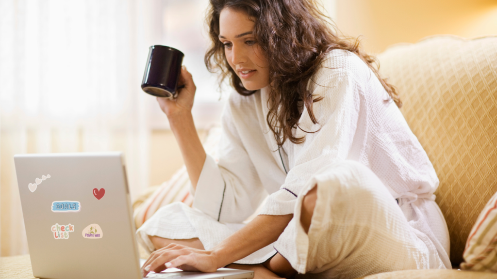 A wedding professional in cozy attire working on business goal setting with a laptop, coffee in hand, and goal-oriented stickers.