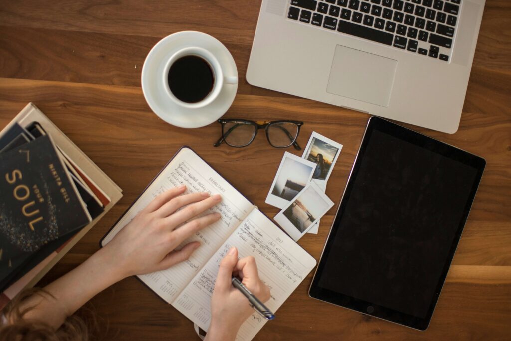 Flat lay of a workspace with a journal, coffee cup, laptop, and photos, symbolizing organized business planning.