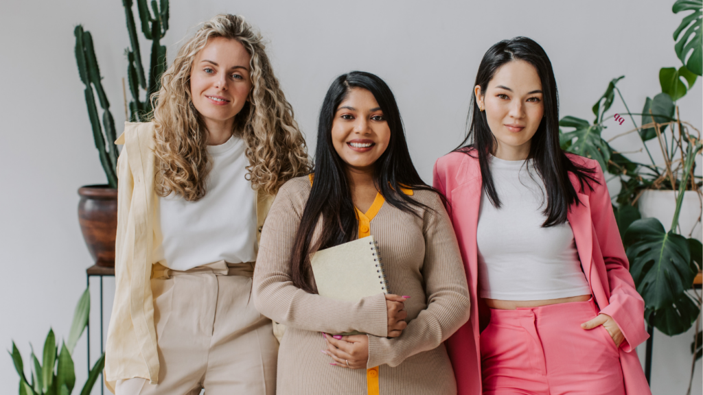 Three professional women smiling and holding notebooks, representing a team of Online Business Managers.