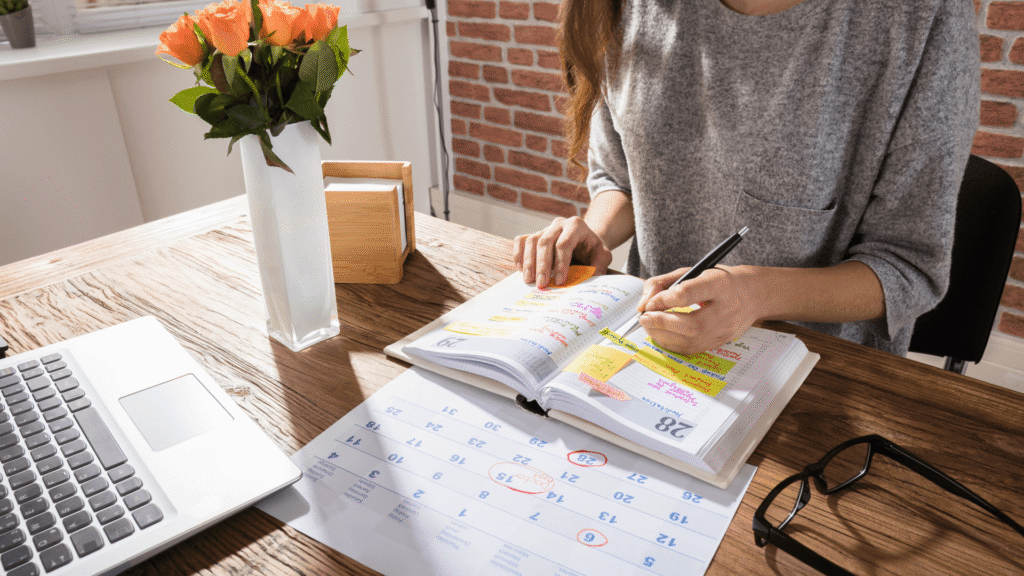 Small business owner reviewing a planner and calendar while creating a quarterly marketing plan for business growth.