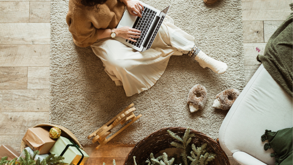 A wedding planner working from home on a laptop surrounded by cozy decor and holiday elements.