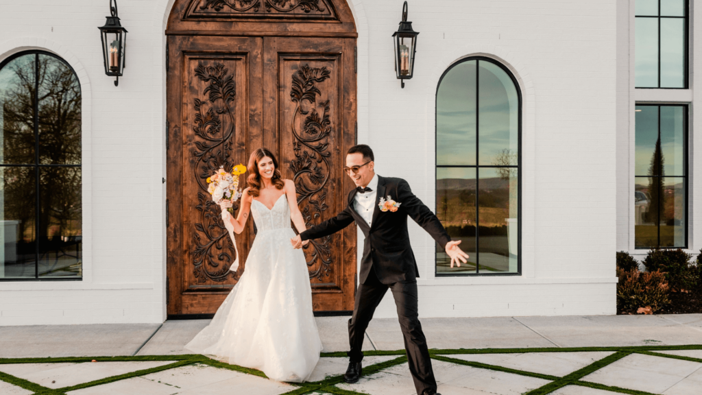 A joyful bride and groom posing in front of an elegant wooden door at a modern California wedding venue.