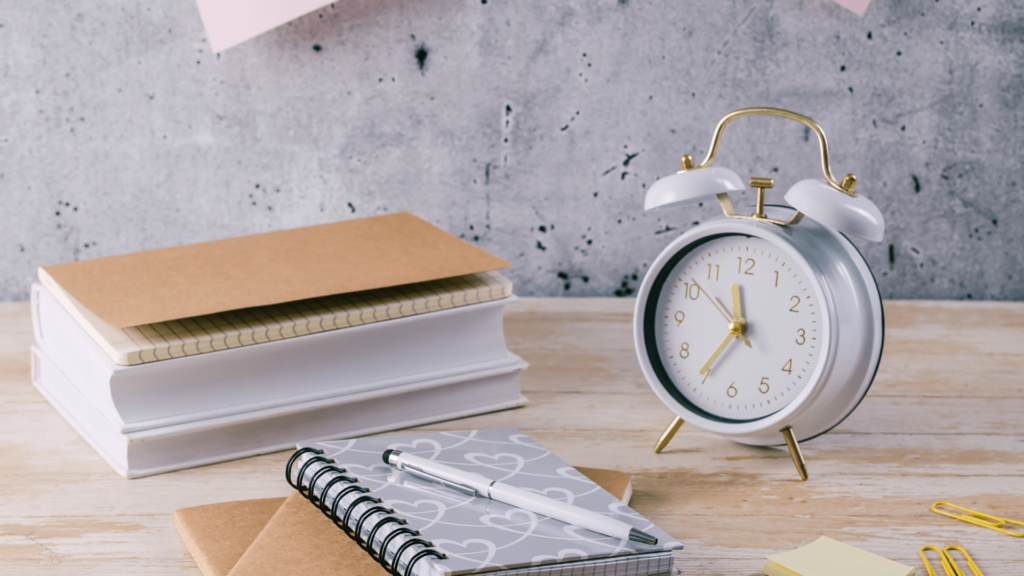 A desk setup featuring a clock, notebooks, and pens symbolizing time management for wedding inquiries.