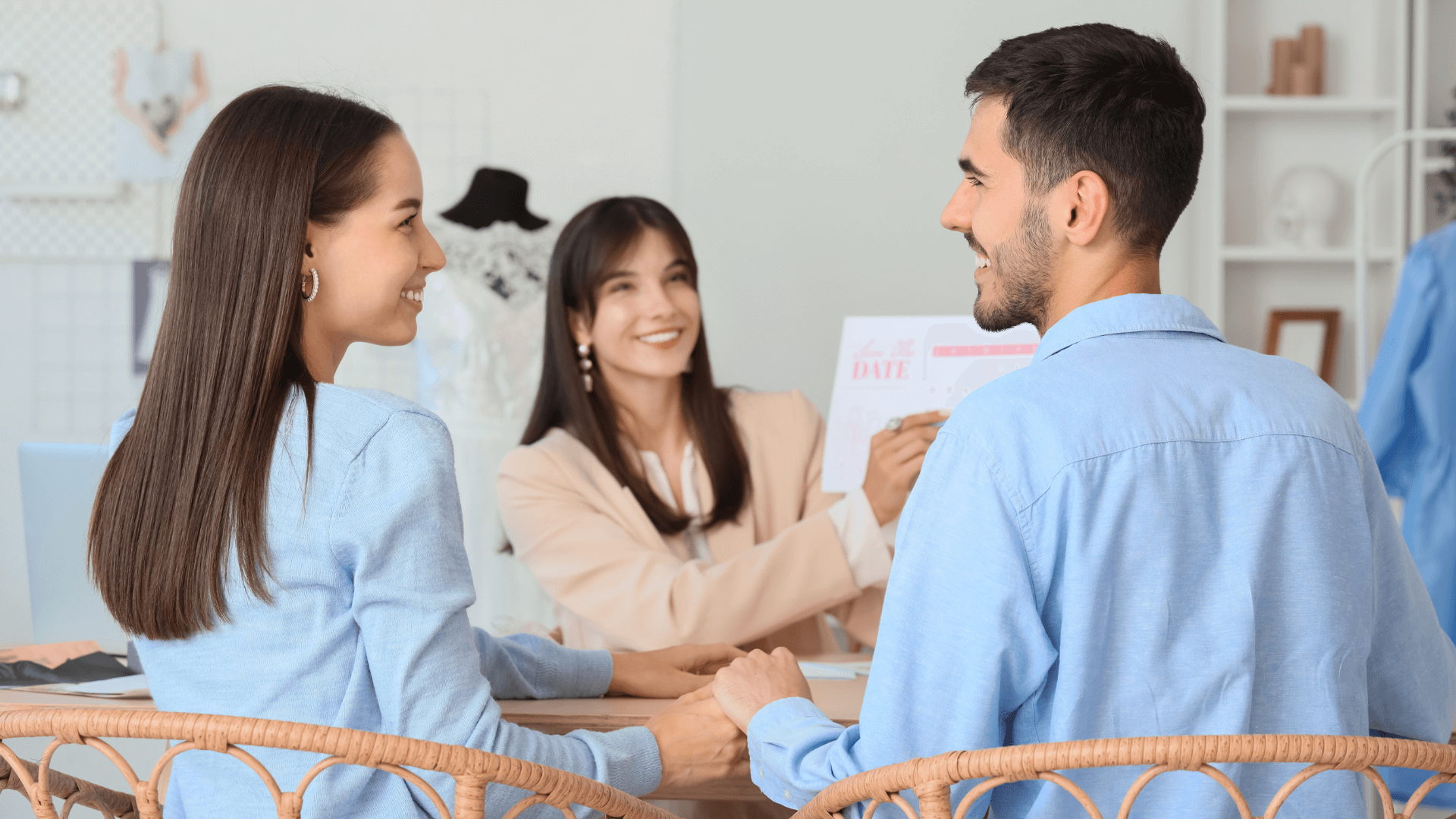 A wedding planner consulting with an engaged couple while holding a save-the-date card.