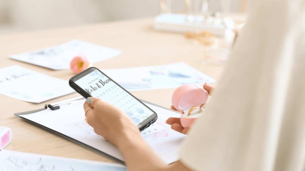 A person using a smartphone for wedding planning while holding an engagement ring case.