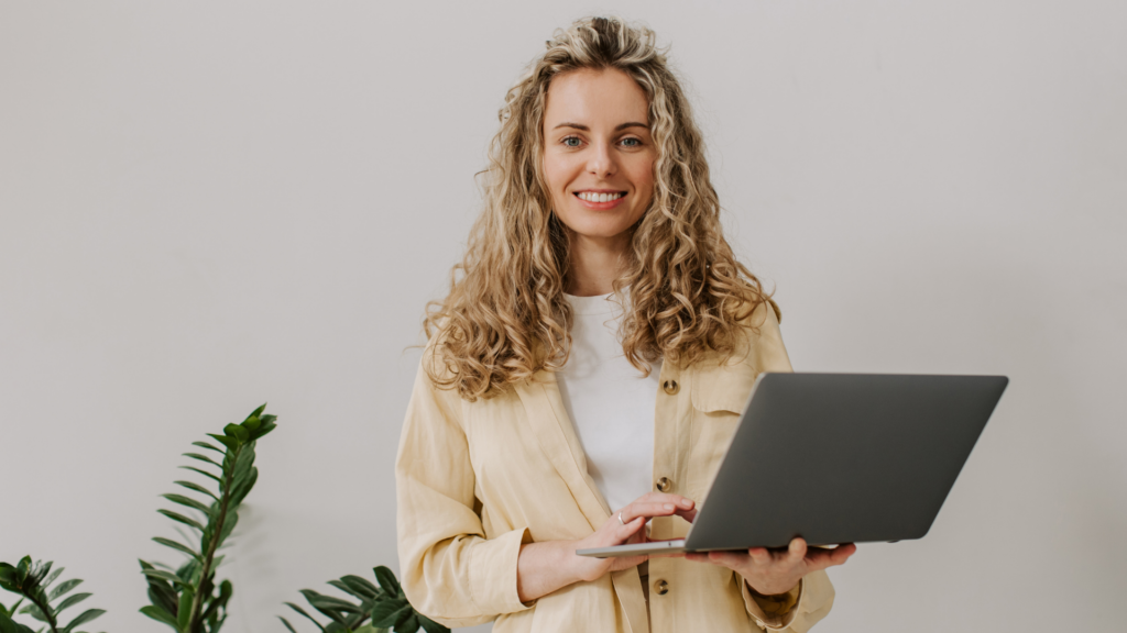 A smiling woman holding a laptop, representing a wedding professional researching online tools like Zola and The Knot for business growth.