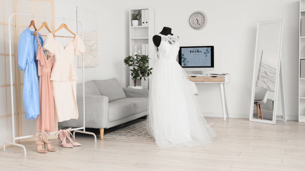 A beautifully styled wedding business workspace with a wedding gown, bridesmaid dresses, and a modern desk setup.