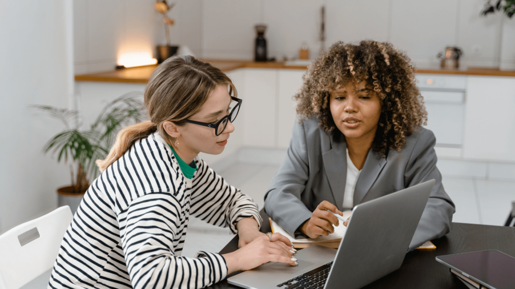 Two women discussing marketing strategy while working on a laptop.