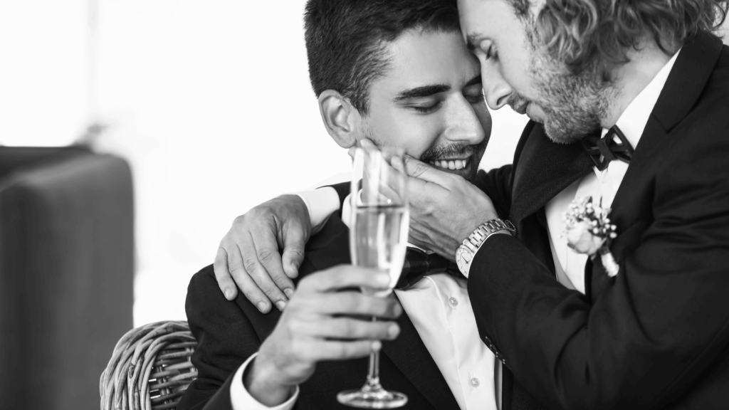 Black and white photo of two men in formal attire toasting with champagne glasses, smiling and celebrating together.