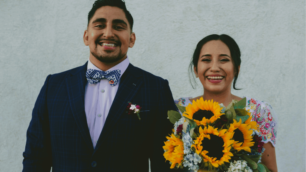 Smiling Mexican wedding couple celebrating with a sunflower bouquet, representing cultural diversity and inclusive marketing in modern weddings.