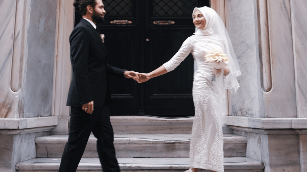A Muslim wedding couple holding hands on marble steps, representing cultural inclusion in modern wedding marketing and PR media features.
