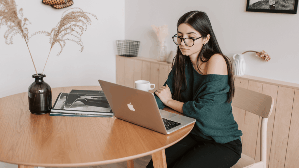 Woman working on a laptop at a wooden table while planning marketing workflows for her creative business