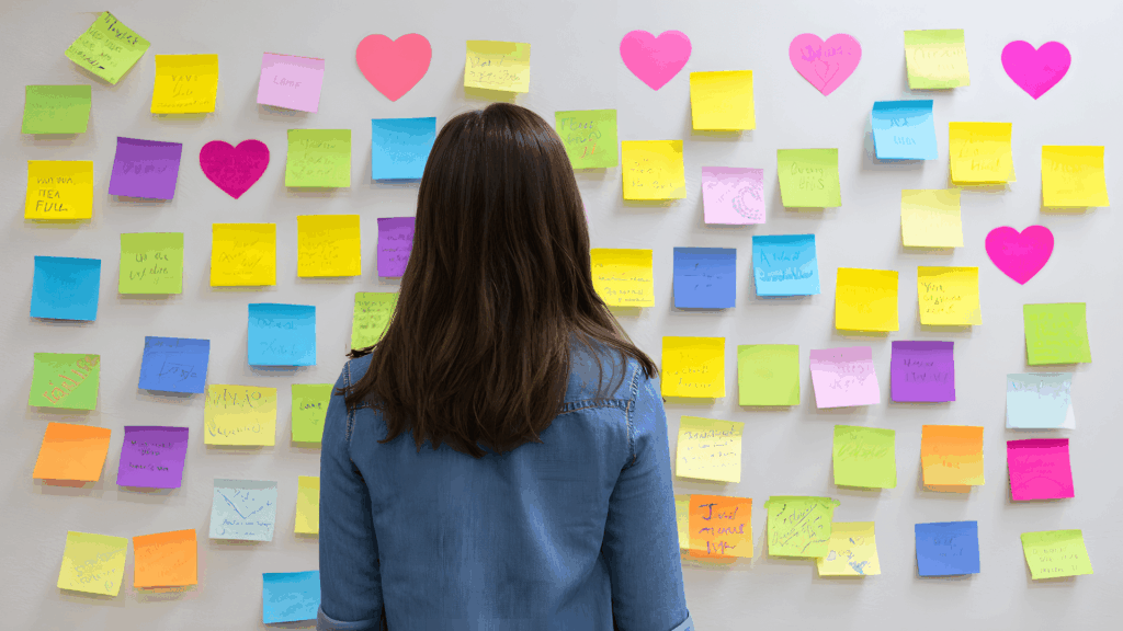 Woman looking at a wall covered in colorful sticky notes while mapping out marketing ideas