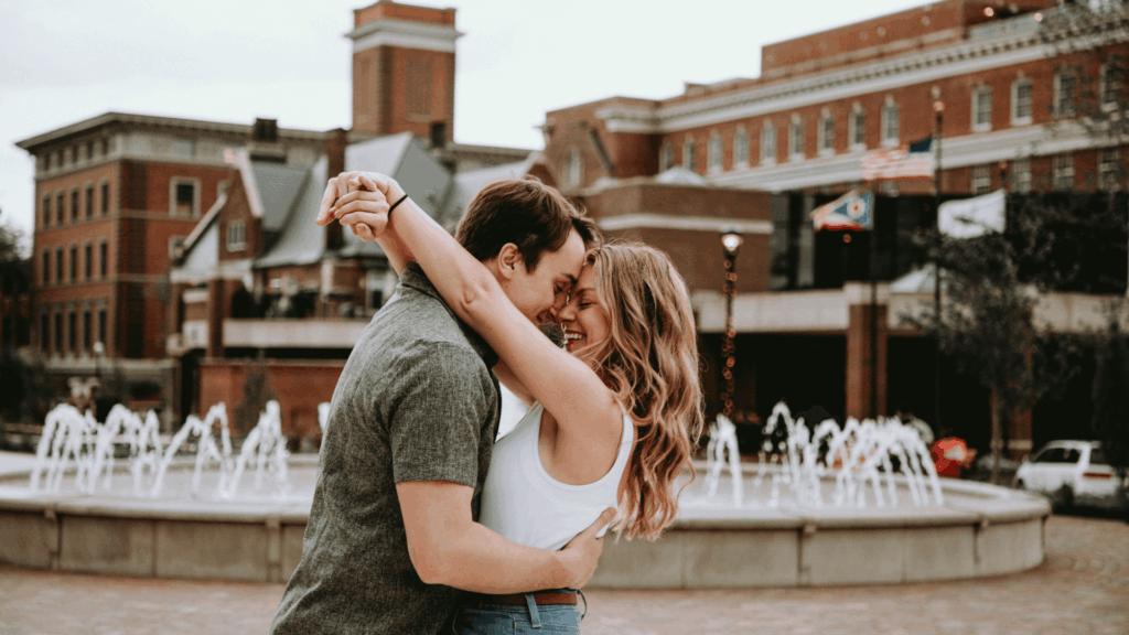 Engaged couple embracing and smiling during an engagement photo session in an outdoor city setting.