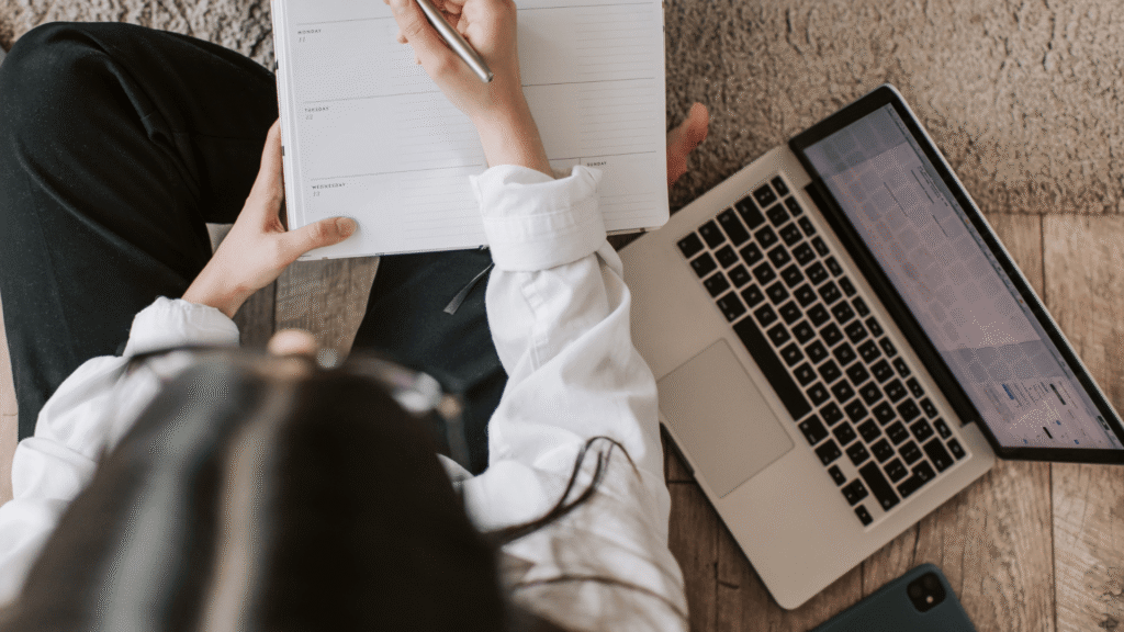 Small business owner planning her marketing system using a weekly planner and laptop.